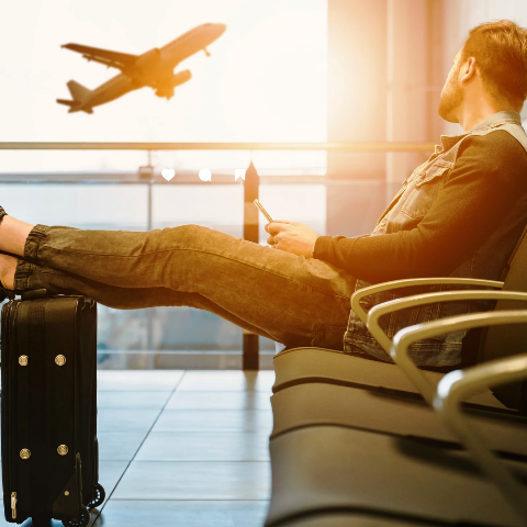 Um homem aguardando seu voo no aeroporto, um avião levantando voo