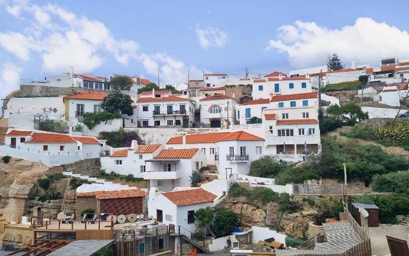 Casas brancas com telhados alaranjados de Azenhas do Mar, em Sintra, Portugal, construídas em camadas sobre a encosta rochosa.