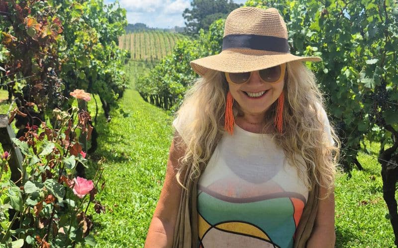 Olivia andando por uma vinícola, com um chapéu e óculos escuros